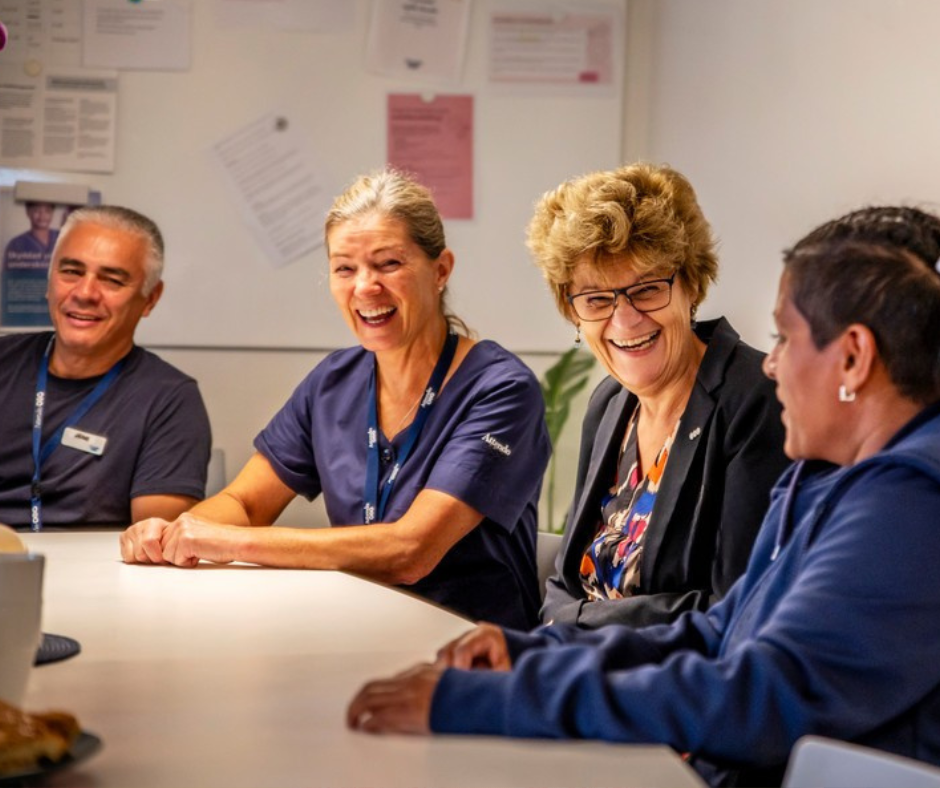 Personer sitter vid ett bord i ett mötesrum, diskuterar vårdrelaterade ämnen och samarbetar