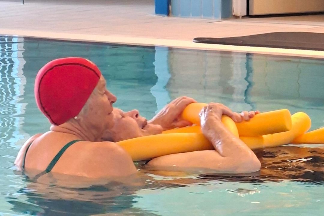 Ingrid flyter i vattnet med hjälp av flytpinne och personal