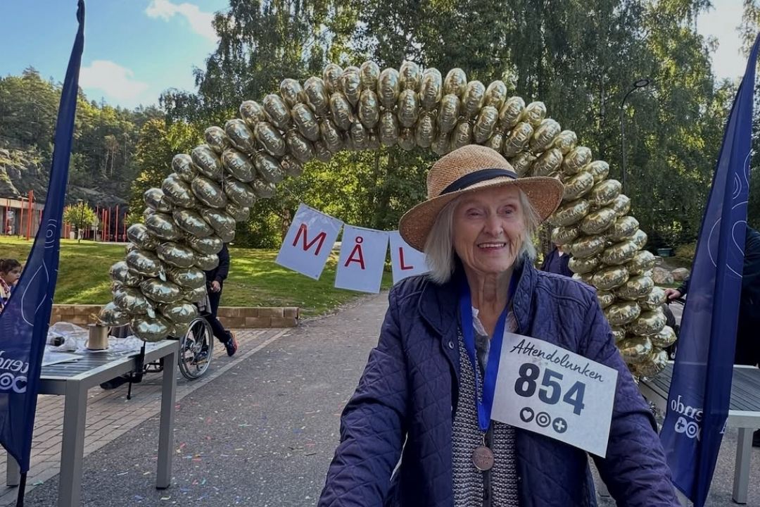&Auml;ldre kvinna med nummerlapp och rullator syns framf&ouml;r m&aring;lg&aring;ngen och en enorm ballongb&aring;ge
