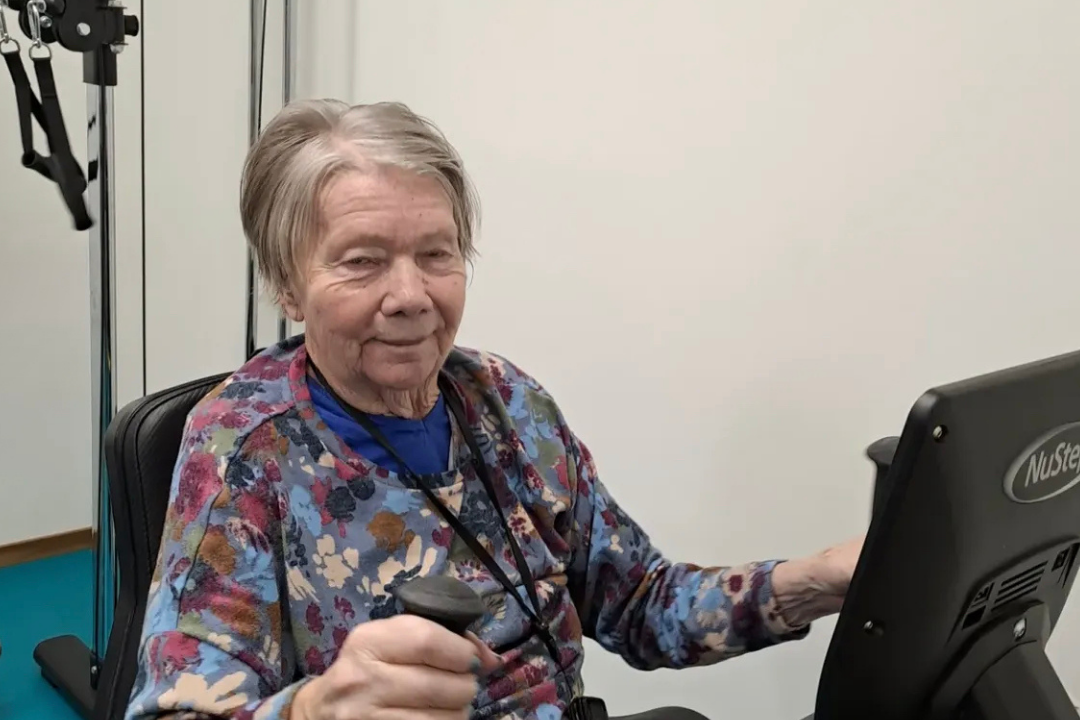 Kvinna från äldreboendet ler och tar i på träningsmaskinen